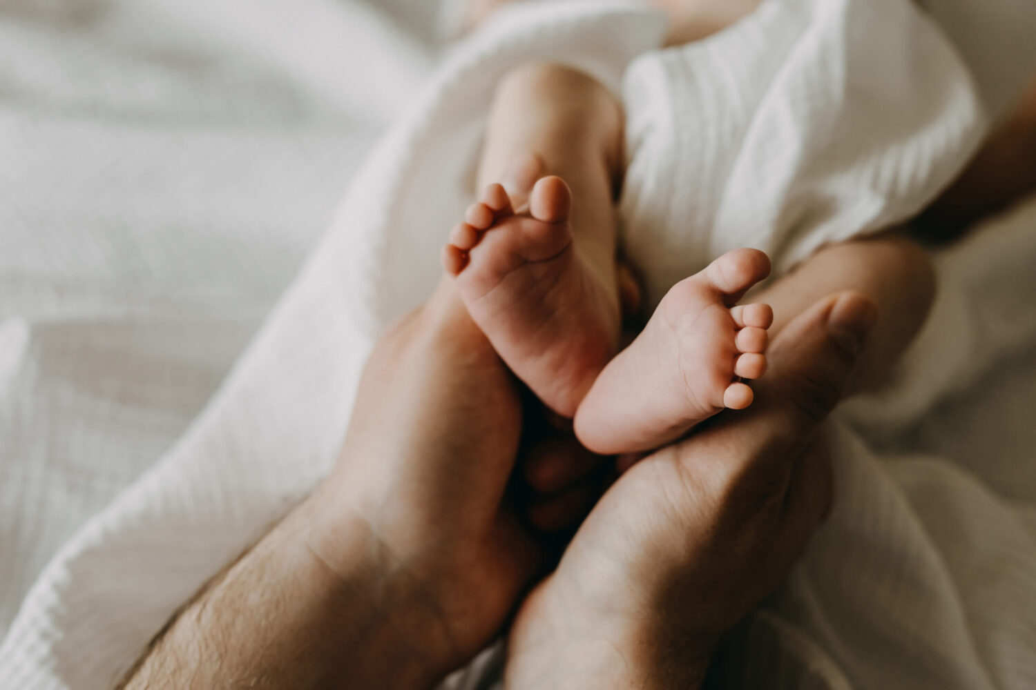 Closeup of father holding small newborn baby feet in hands.